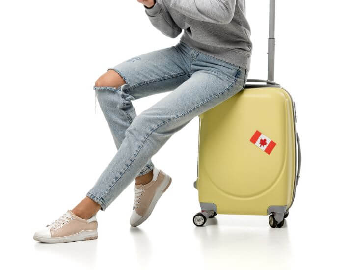 A girl sitting on top of her suitcase. there is a canadian flag on the suitcase