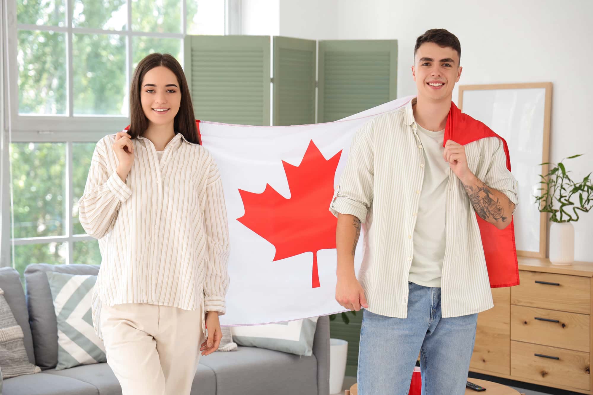 A couple holding a Canadian flag, representing the concept of spousal sponsorship in Canada, as they smile in a cozy home setting.